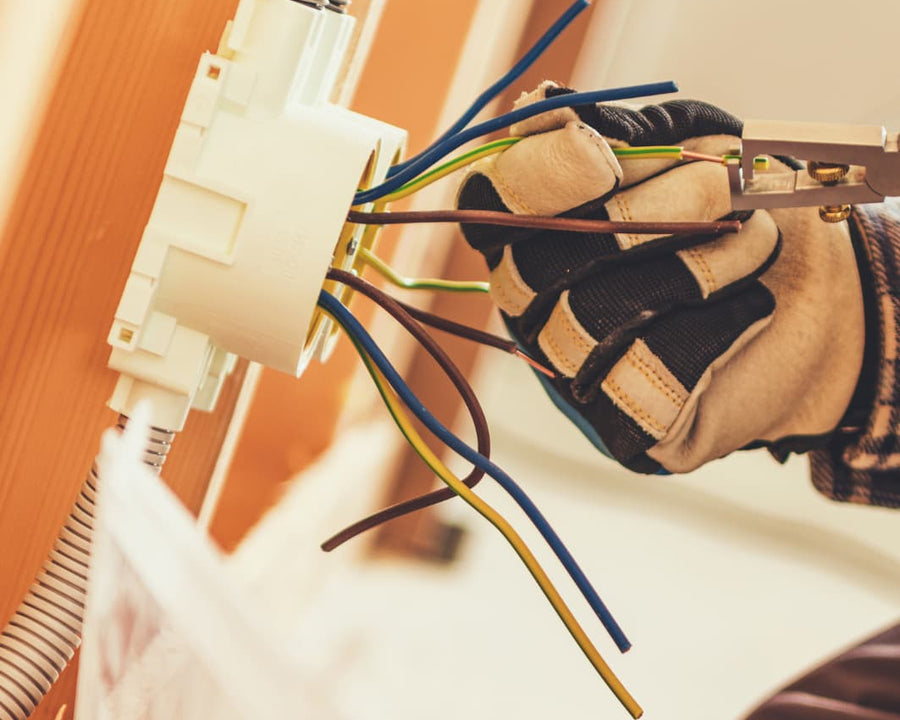 Une main gantée avec un dénuder sur des cables électriques